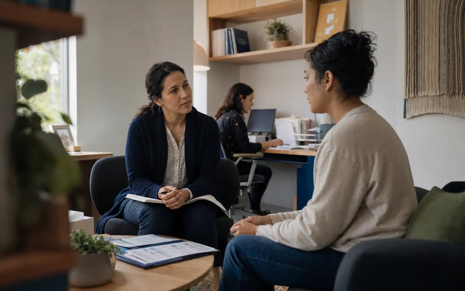 A clinician and a patient talking across a small table in a community health office.