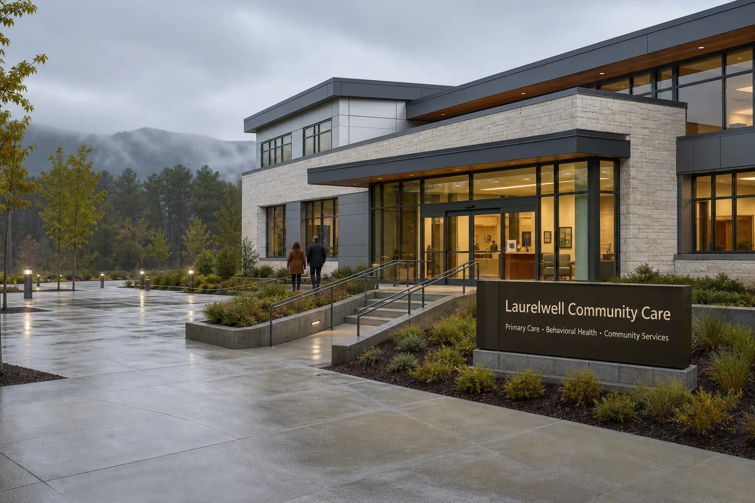 Contemporary community healthcare center with a glass entrance, accessible ramp, and Laurelwell Community Care signage, set against a quiet wooded ridgeline